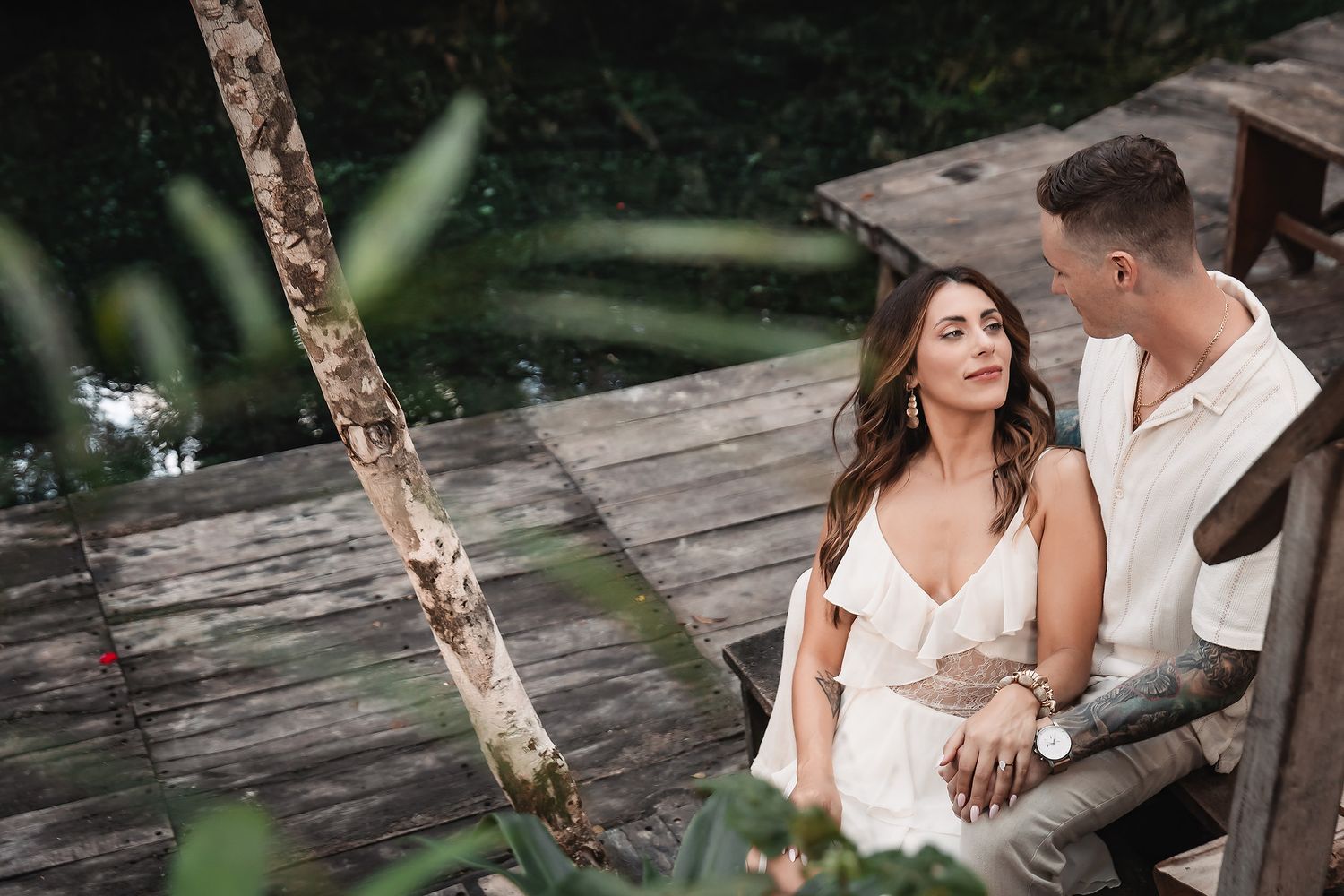 Romantic photoshoot on rustic wooden platform surrounded by lush greenery.