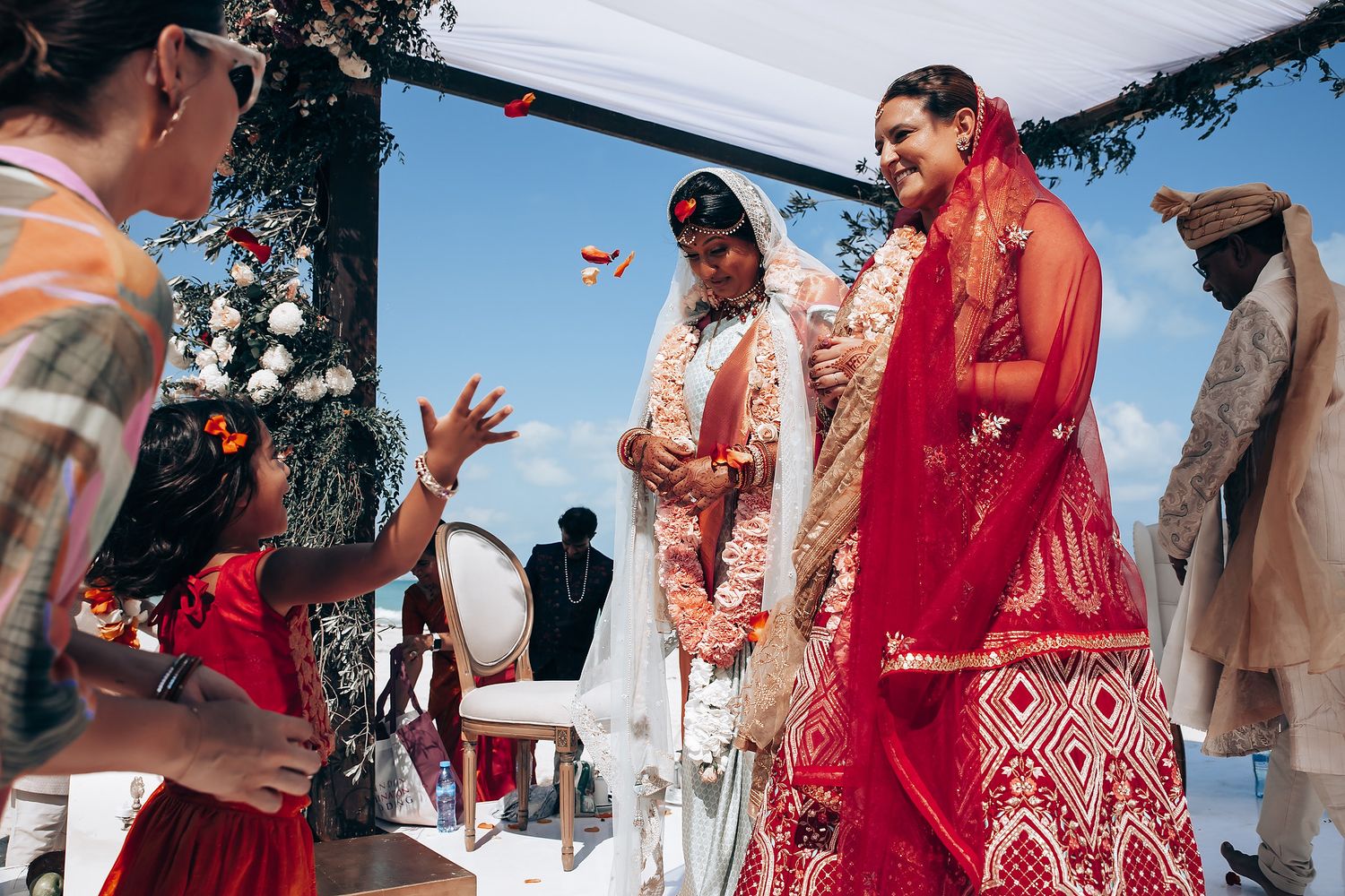 Traditional Indian wedding ceremony with red and coral decor elements by the ocean.