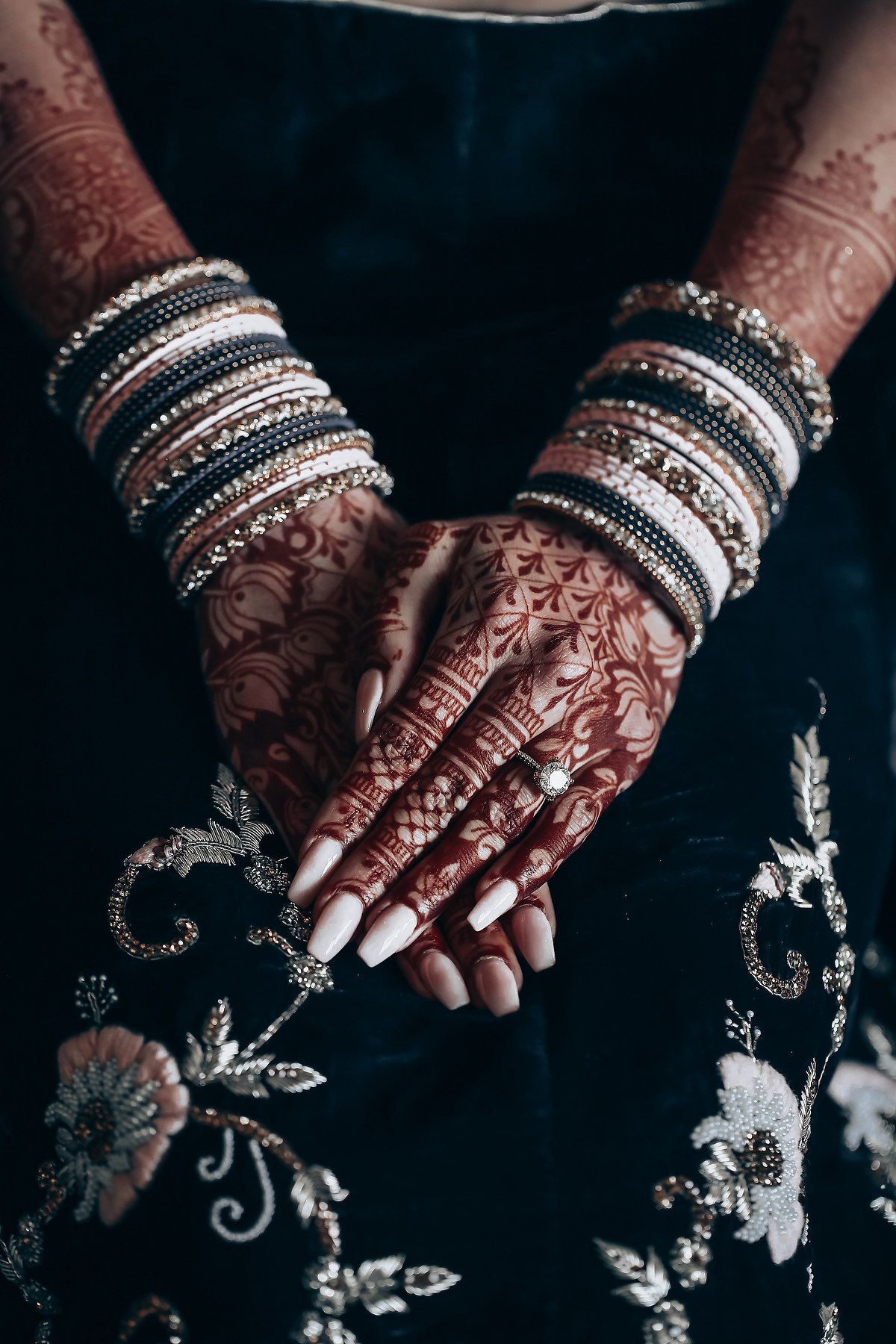 Close-up of henna adorned hands with white and silver wedding bangles.