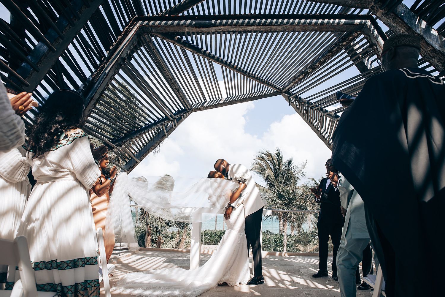 Panoramic view of an outdoor wedding ceremony with guests seated under a geometric shade structure.