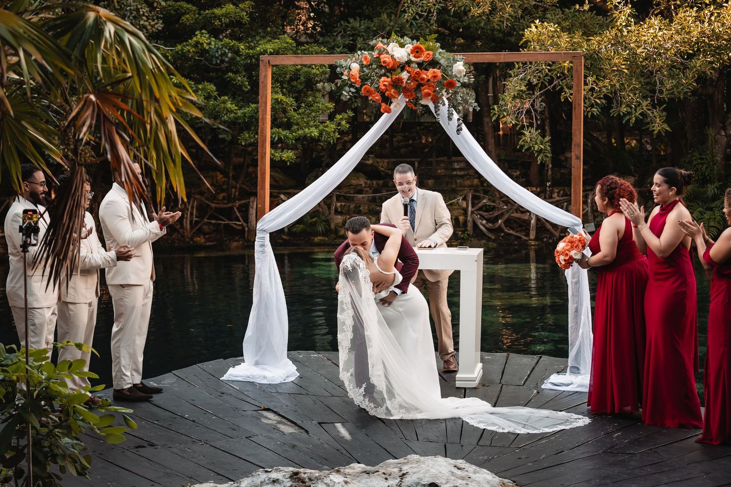 Wedding party arranged on wooden deck during outdoor ceremony with burgundy and white color scheme.