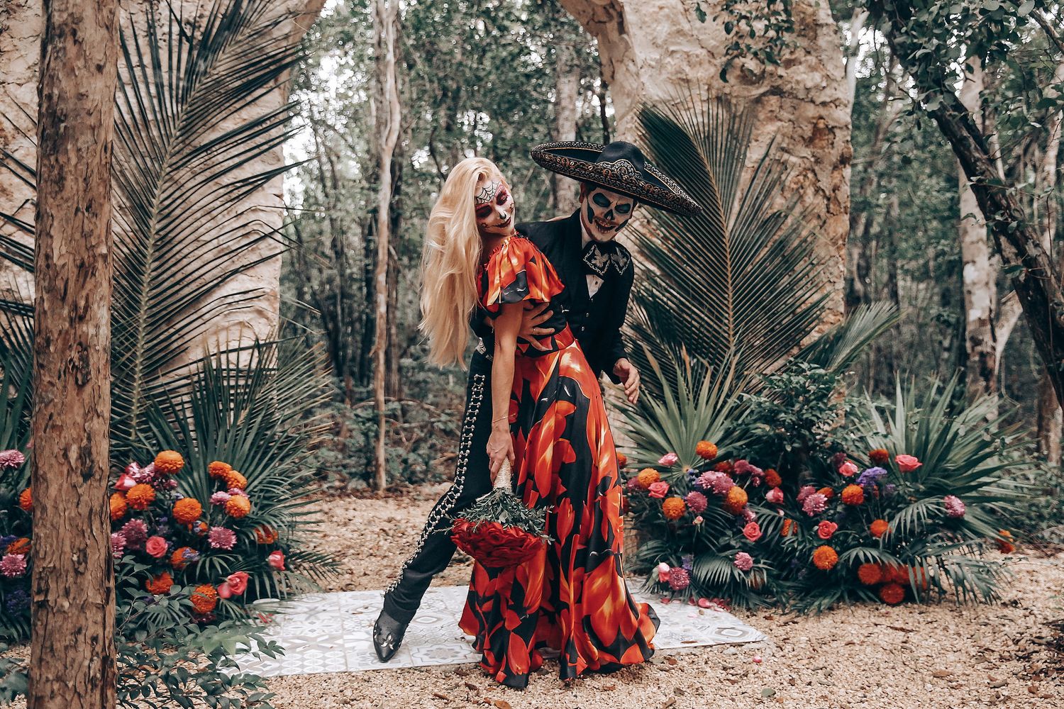 Forest wedding venue with palm fronds and red floral arrangements along stone pathway.