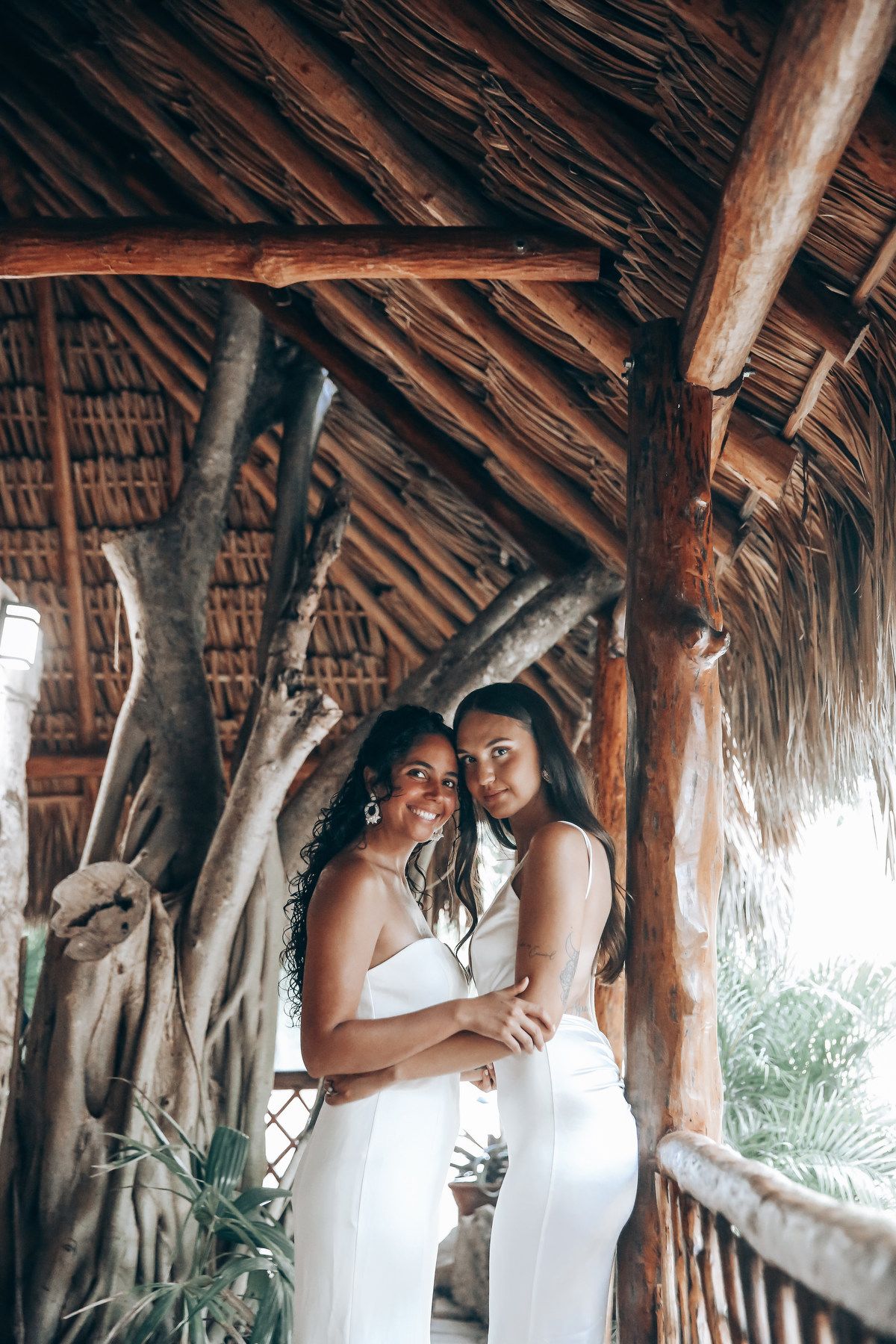 A couple shares a romantic moment under a rustic thatched-roof palapa structure.