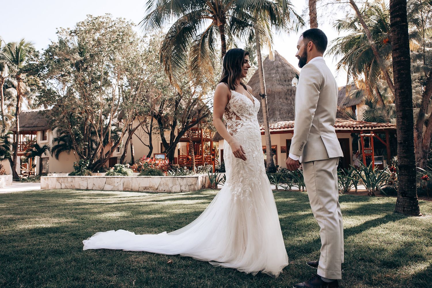 Wedding ceremony setup in a tropical garden with palm trees and guests in white attire.