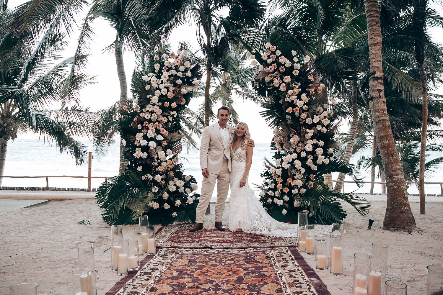 Wedding ceremony setup on beach with floral arch and palm trees.