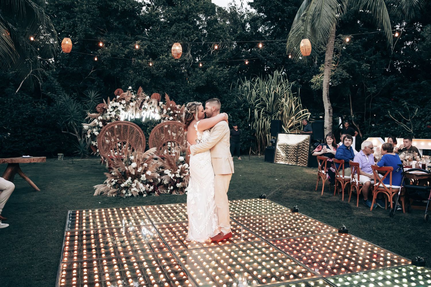 Newlyweds share their first dance on a glowing LED dance floor surrounded by lush tropical greenery.