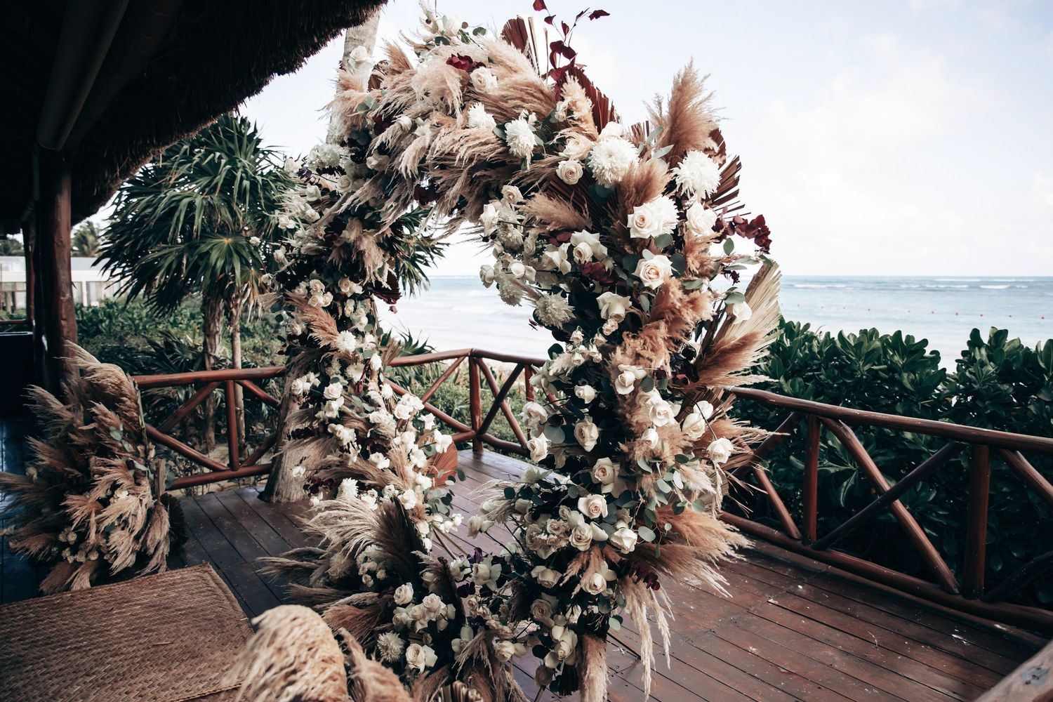 A stunning circular wedding arch adorned with white roses and pampas grass overlooking a tropical ocean backdrop.