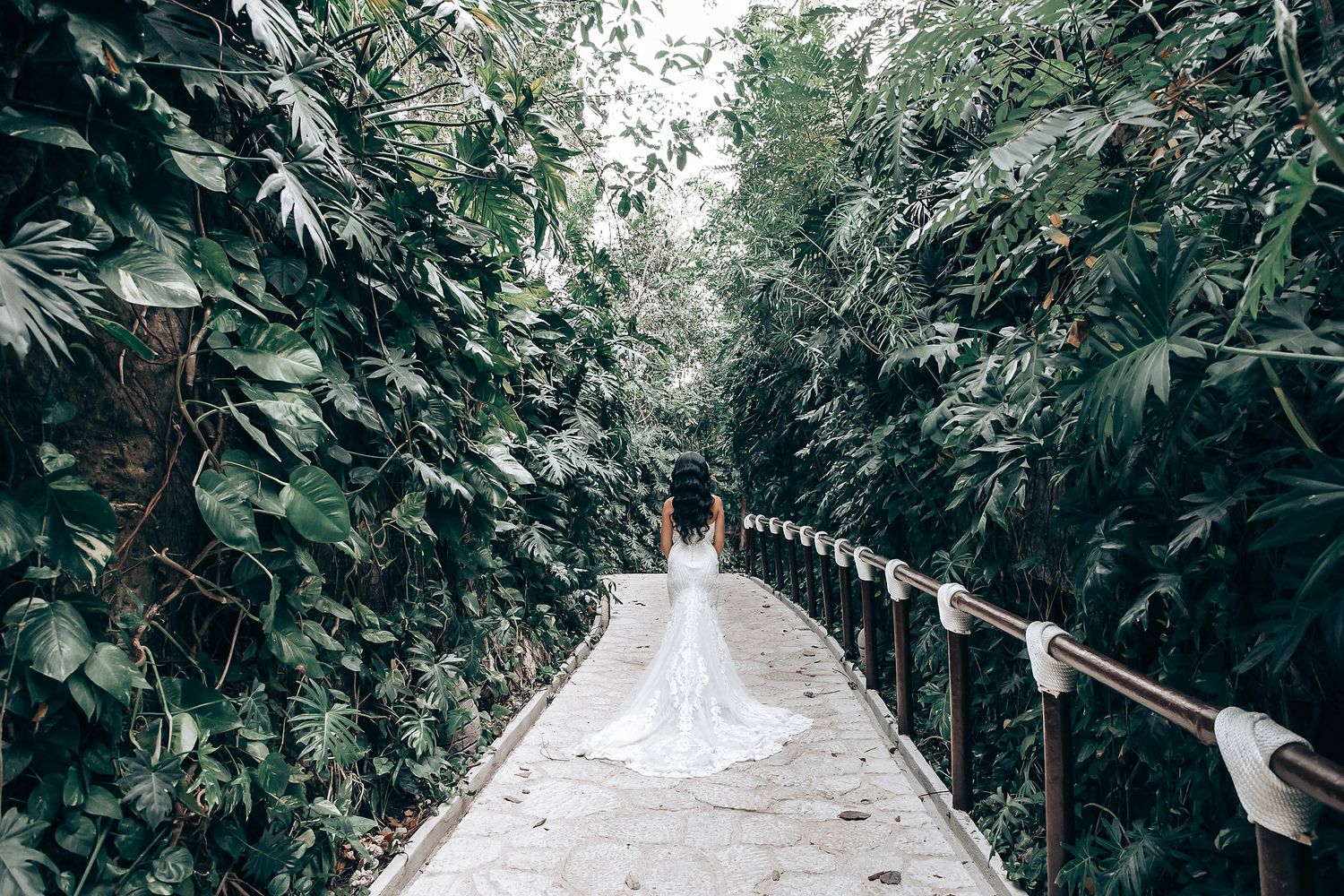 Wedding ceremony path lined with lush tropical greenery and white floral arrangements.