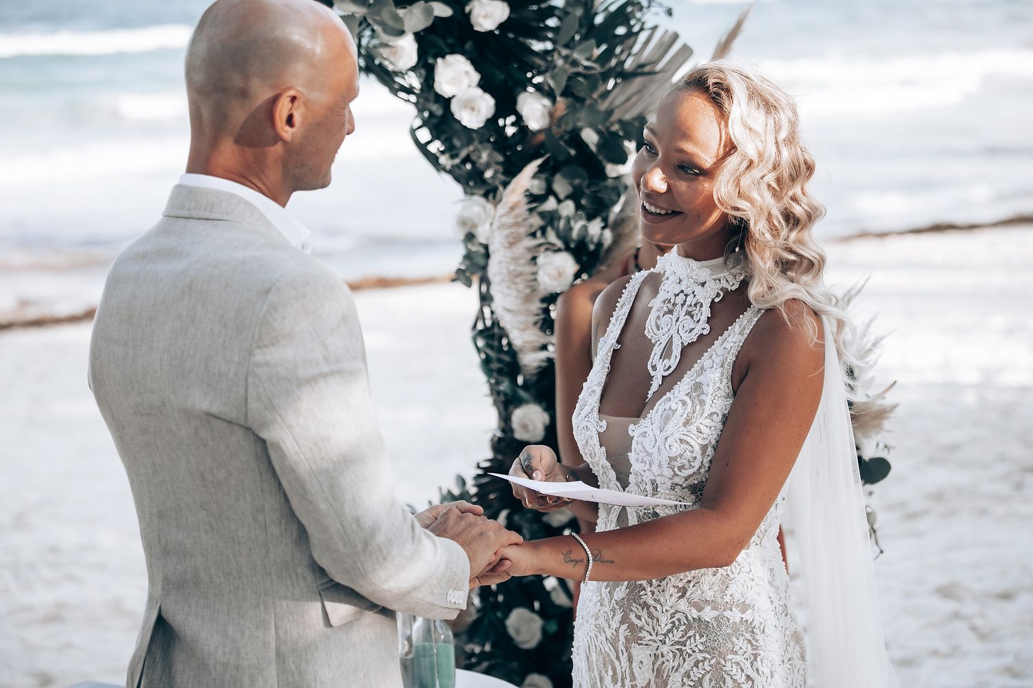 Couple exchanging vows during beach wedding ceremony with decorated arch.