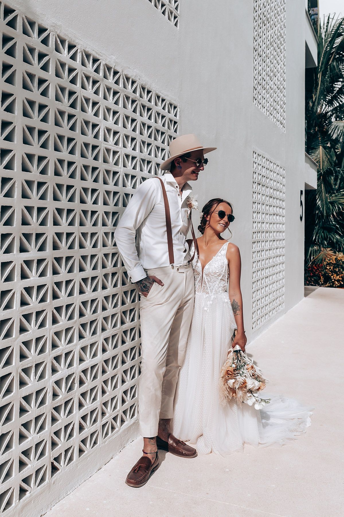 A stylish wedding couple posing against a geometric white wall pattern.