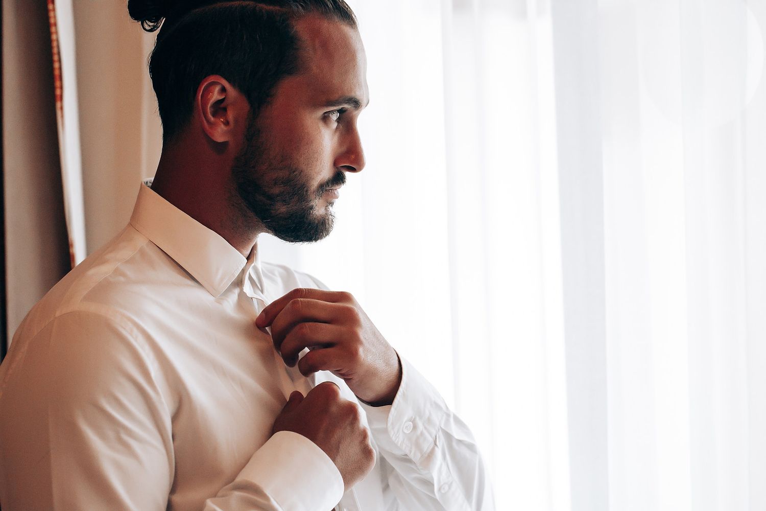 A person in a white button-down shirt stands against a bright window background.