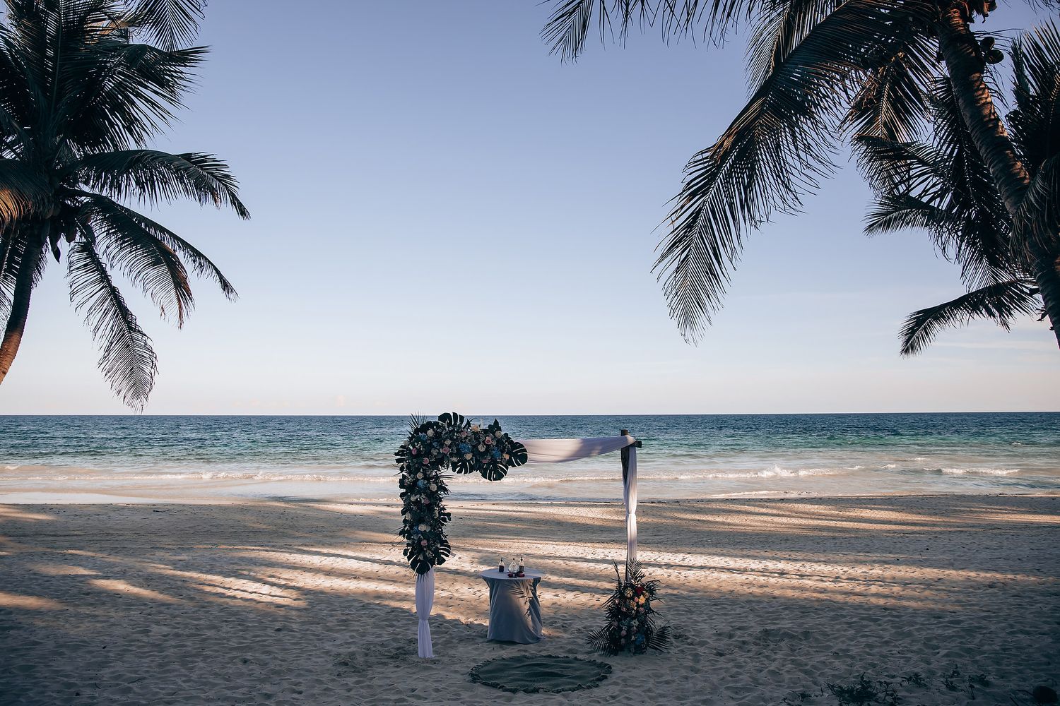 A tropical beach with palm trees and a person walking on the sand.