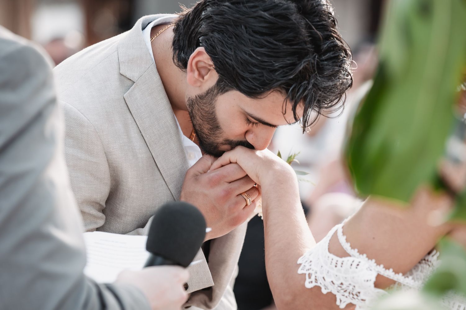 Groom tenderly kisses bride's hand during intimate beach wedding ceremony exchange.