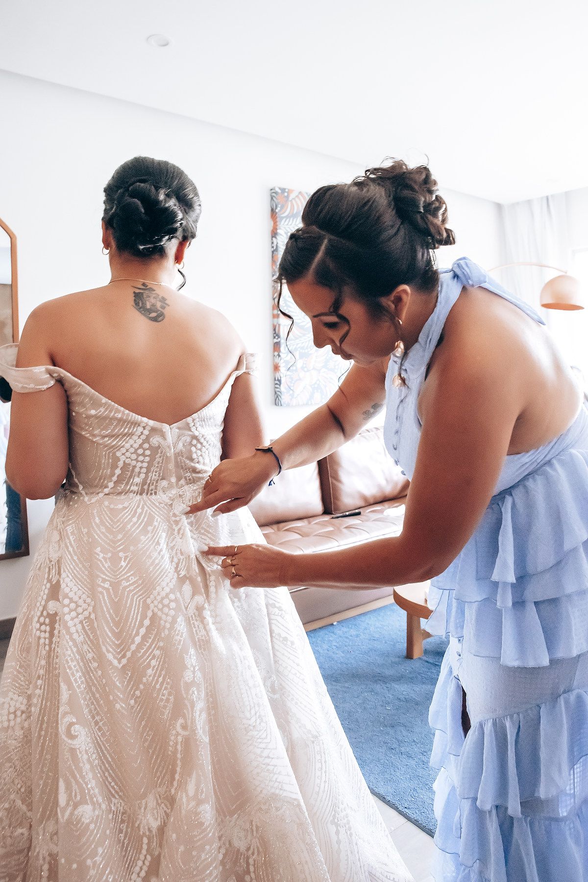 Close-up view of a white beaded wedding dress being laced up and adjusted by helpers.