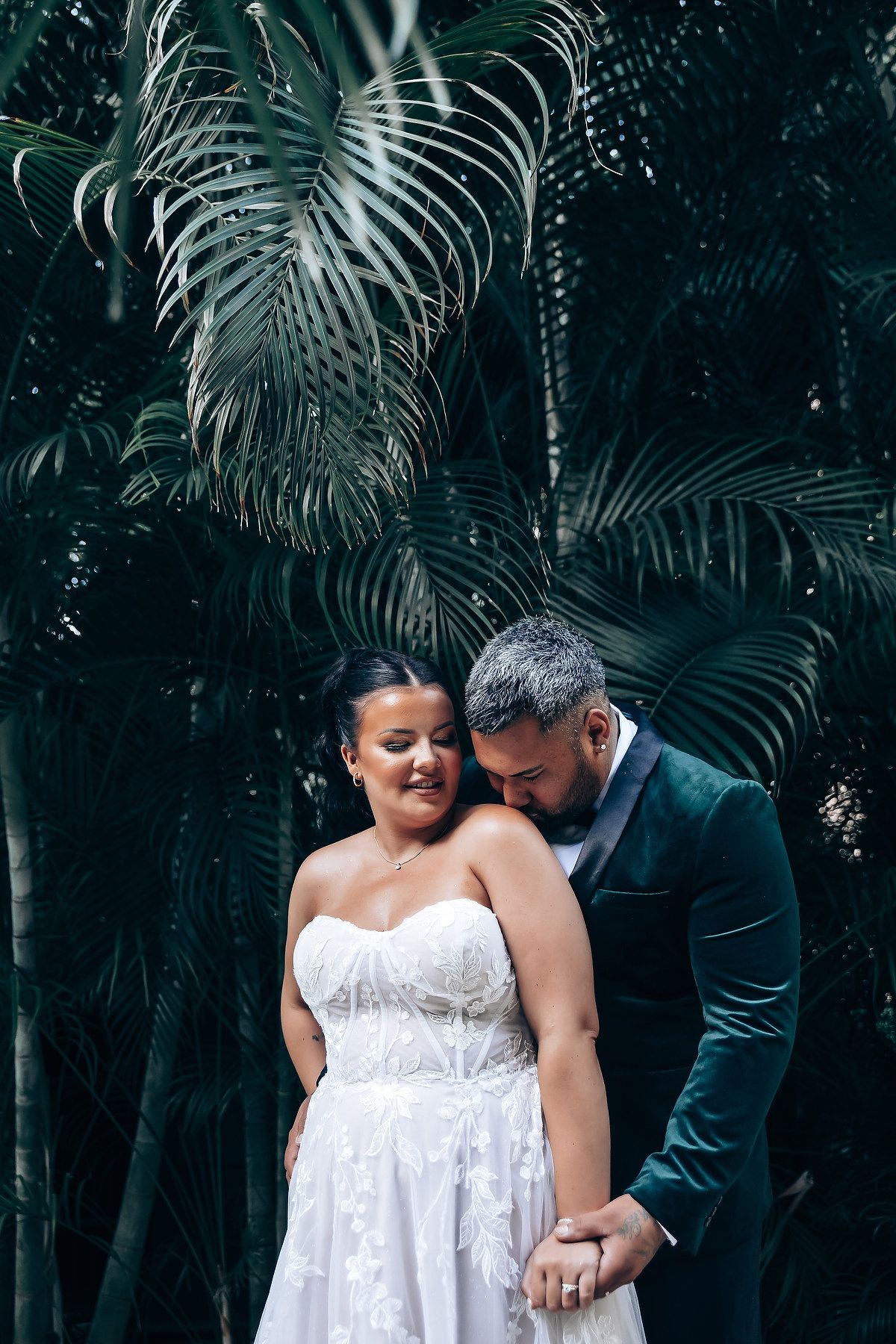 Intimate wedding portrait among tropical palm fronds in garden setting.
