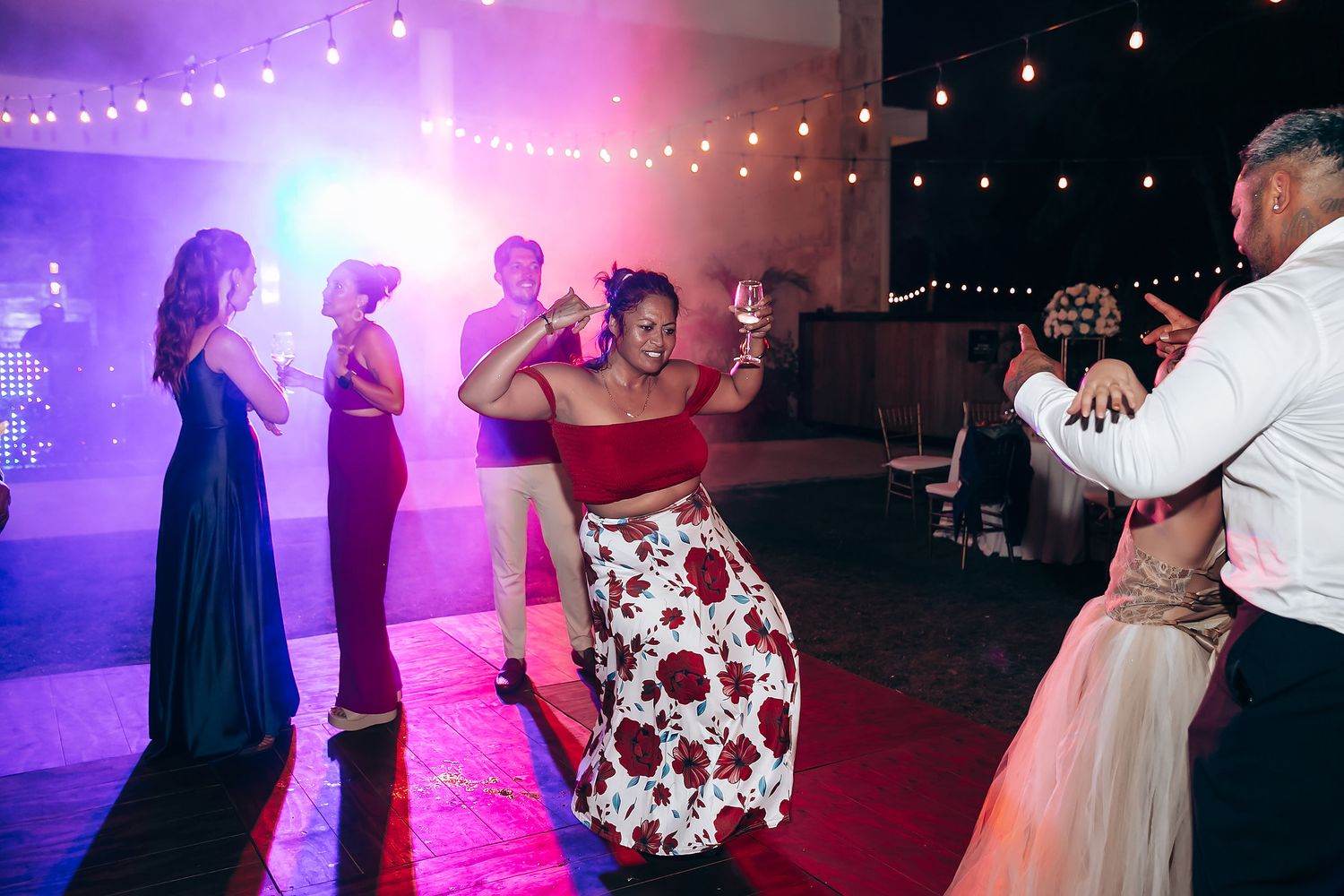 Wedding reception dance floor lit with purple lighting and string lights overhead.