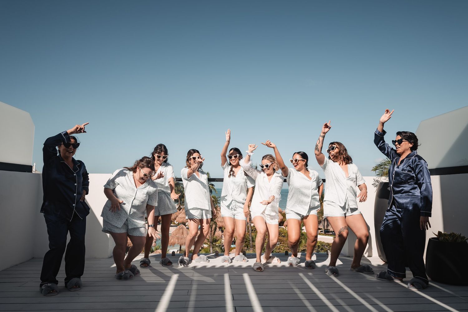 Group of women in matching white outfits celebrating on a rooftop terrace under a clear blue sky.