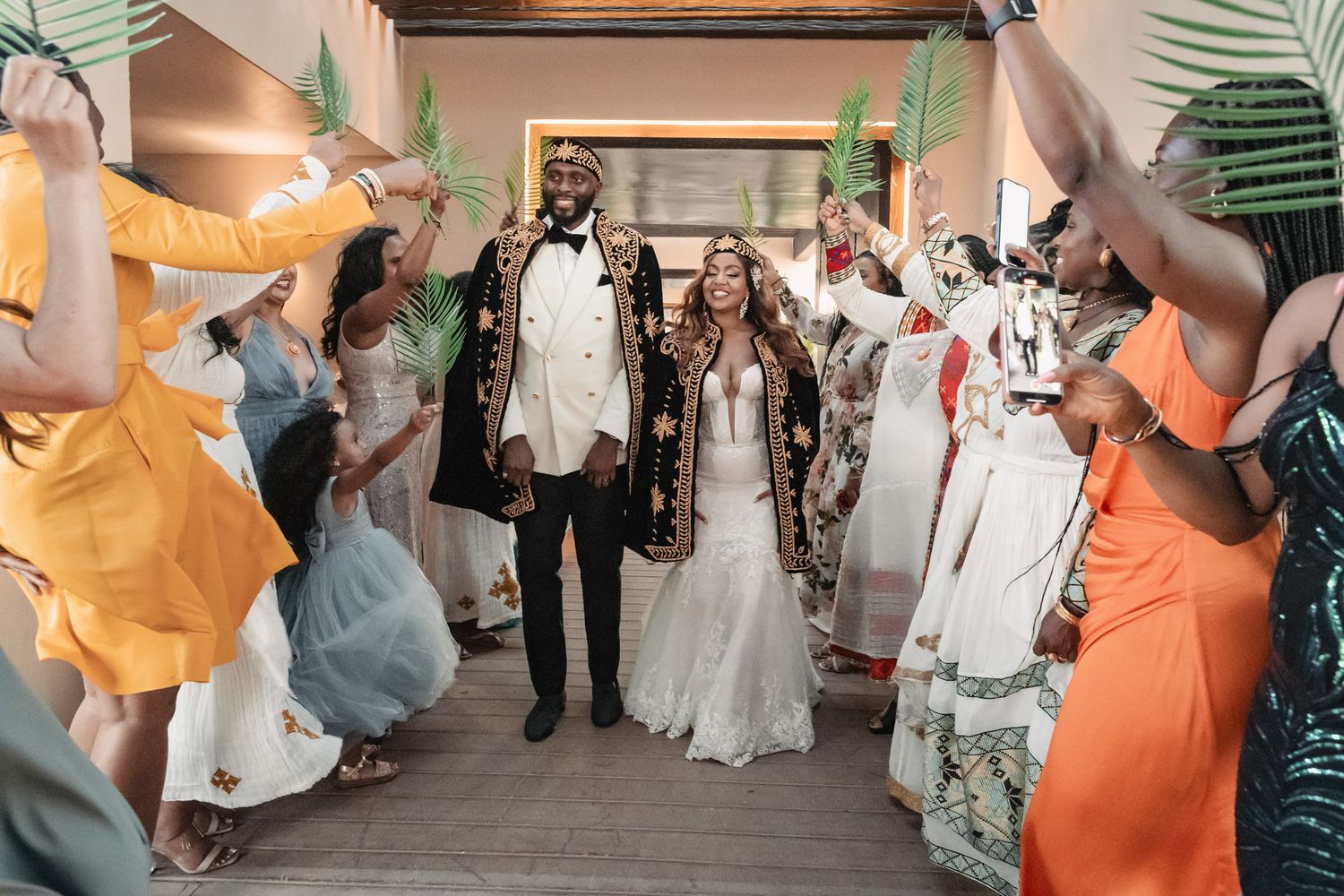 Newlyweds walk through a joyful exit tunnel of guests waving tropical palm leaves.