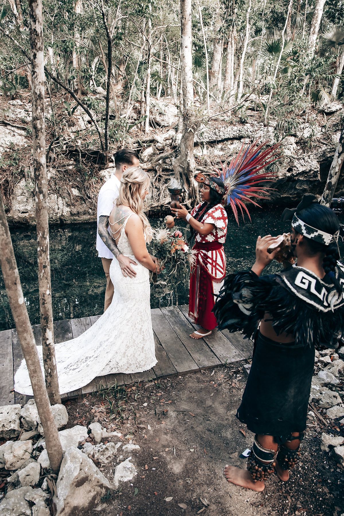 Traditional ceremony in a lush forest setting with performers in ceremonial dress and feathered headdresses.