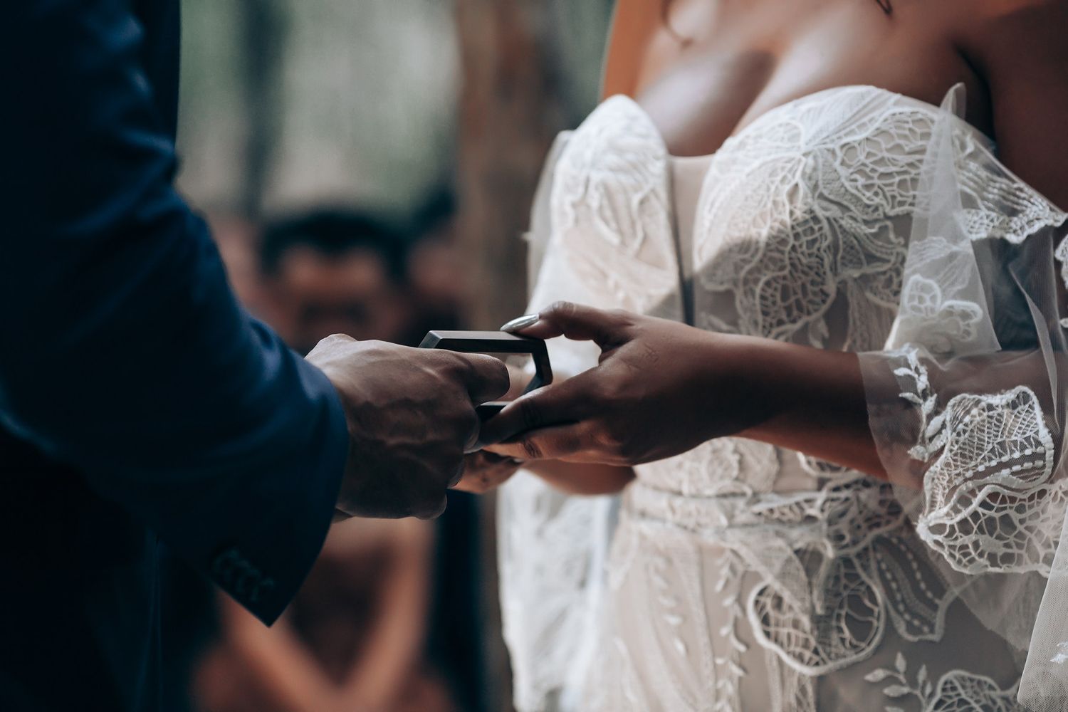 Close-up detail of intricate lace wedding dress during outdoor ceremony.