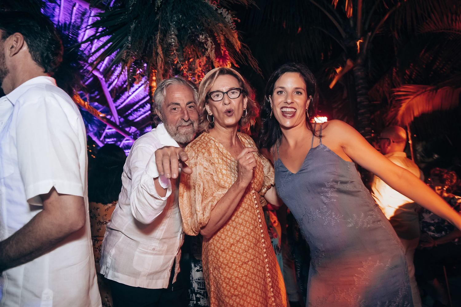 Party guests enjoying themselves under purple-lit palm trees at a nighttime celebration.