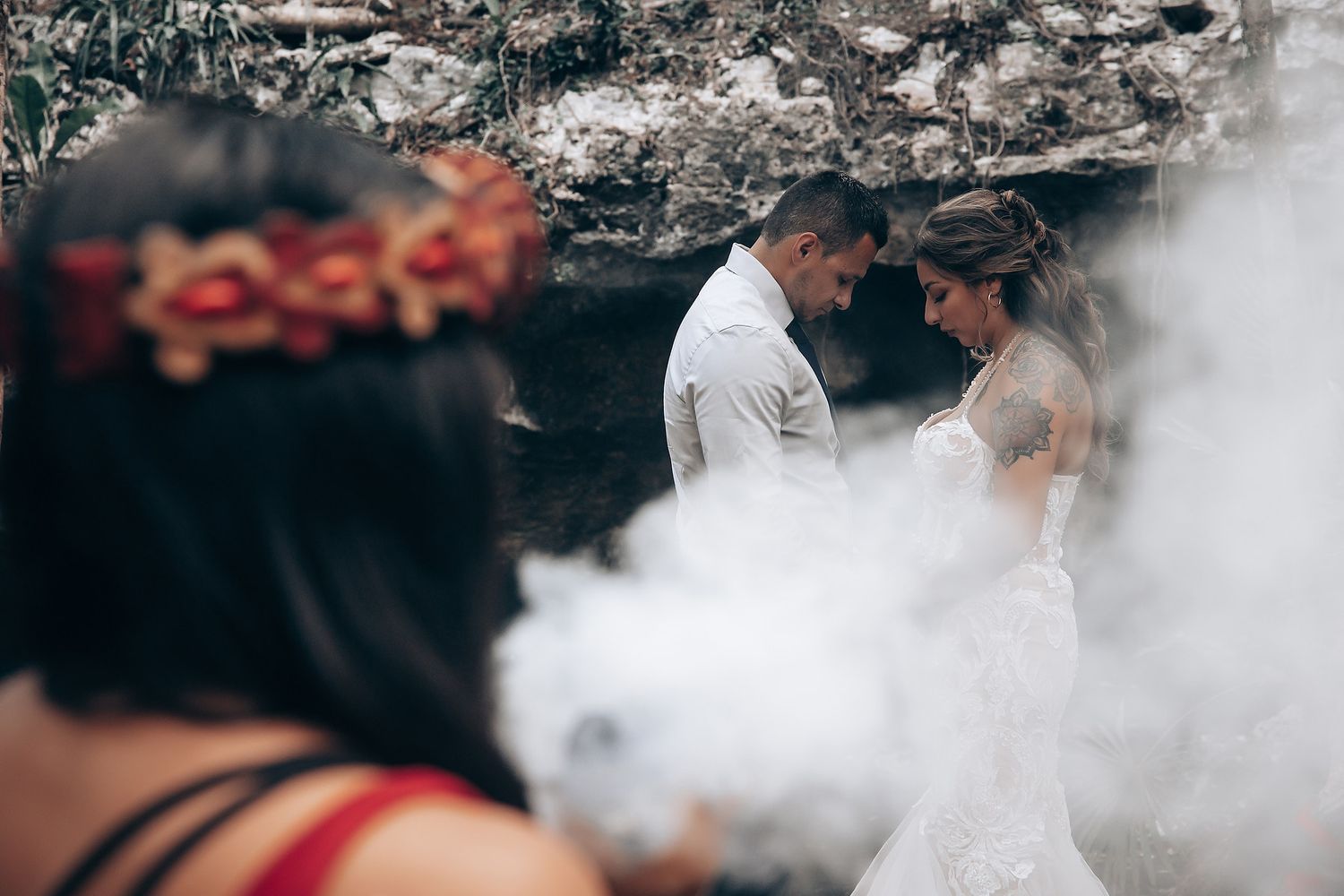 A couple embraces in a cloud of white smoke during an outdoor wedding photoshoot.