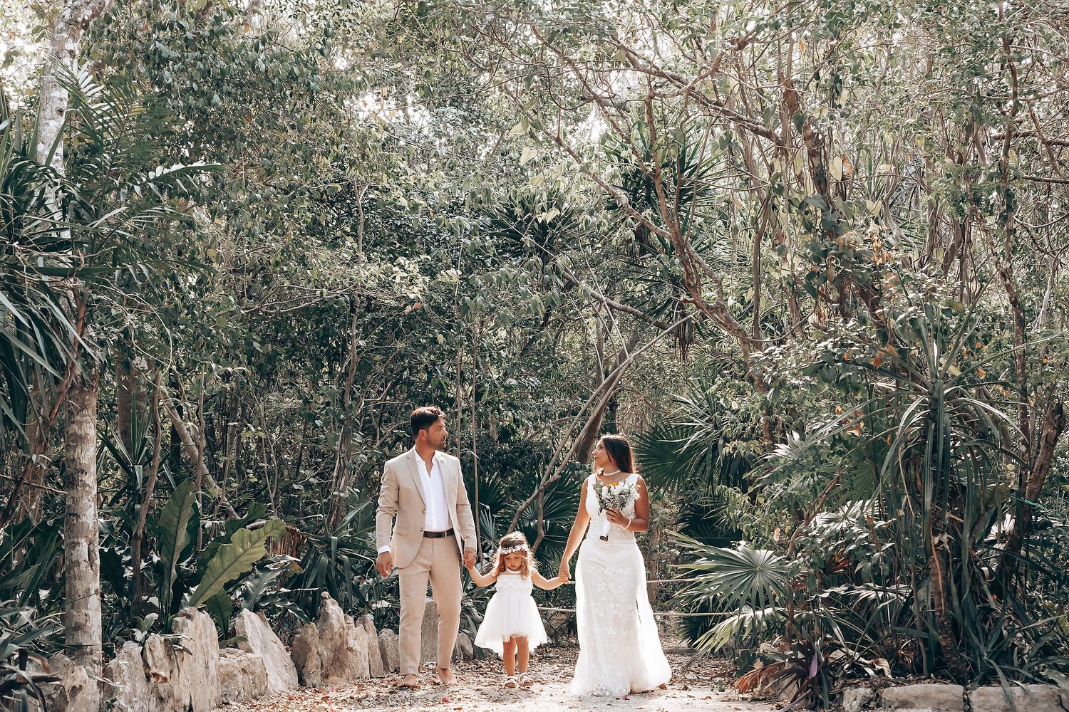 A romantic couple walks together through a lush tropical forest path with sunlight filtering through the trees.