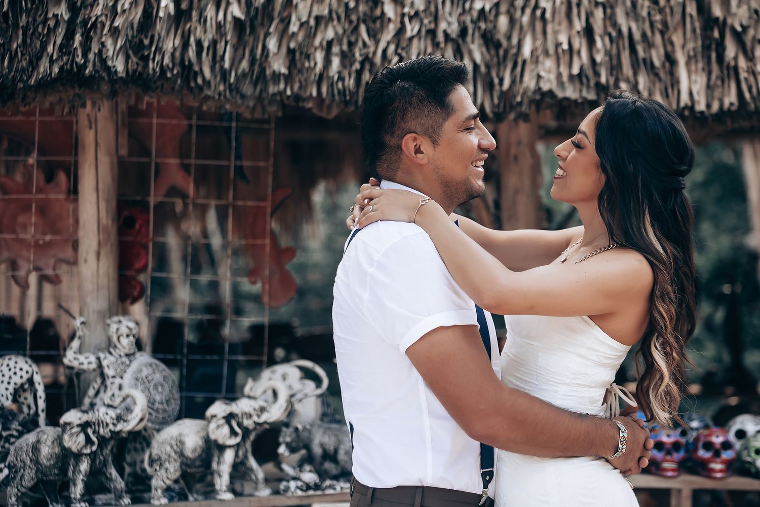 Couple in white outfits dancing together in romantic poses against a rustic backdrop with string lights.