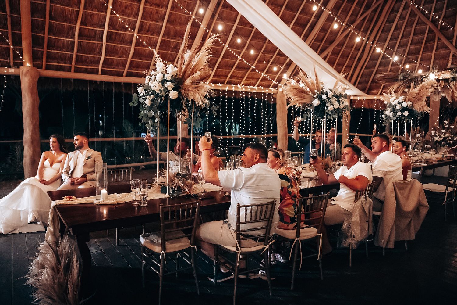 Wedding reception celebration inside a rustic barn venue decorated with warm string lights and exposed wooden beams.