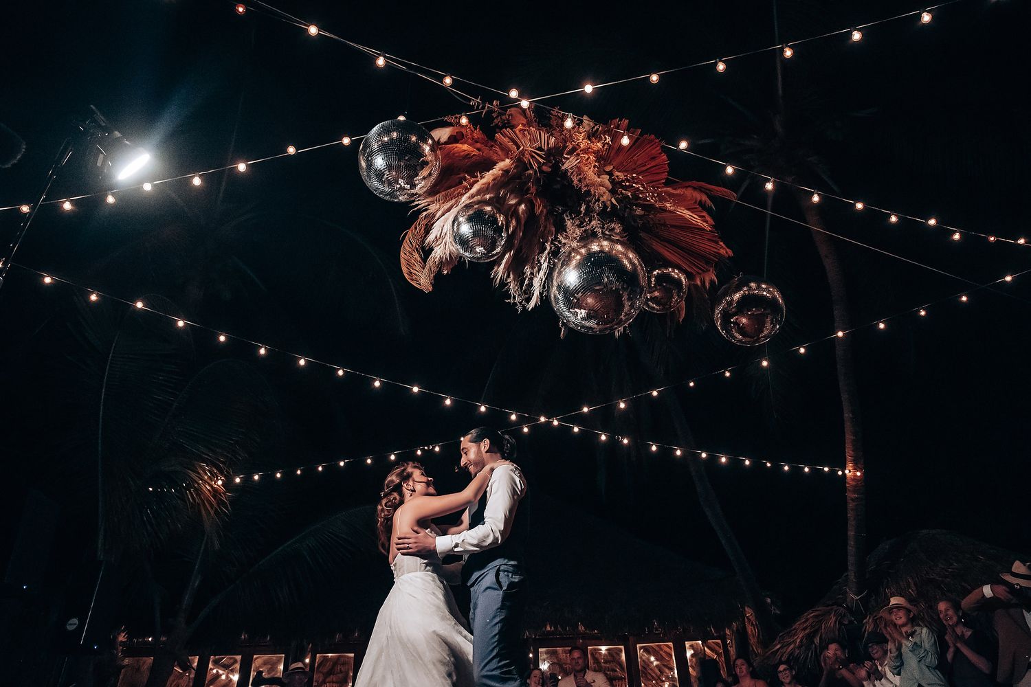 String lights and disco balls illuminate a romantic outdoor evening wedding reception.