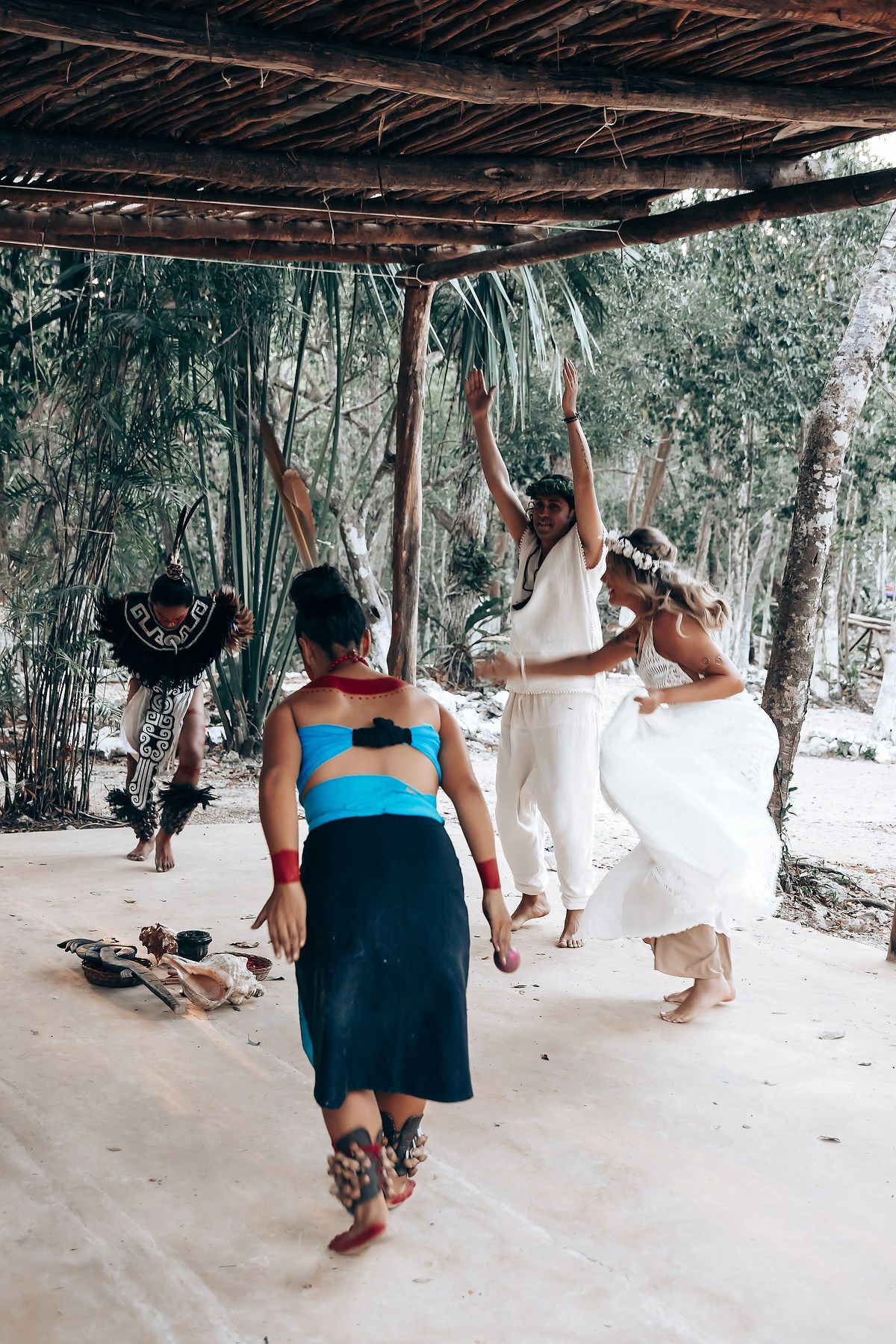 People dancing and enjoying themselves under a rustic covered patio area surrounded by tropical vegetation.