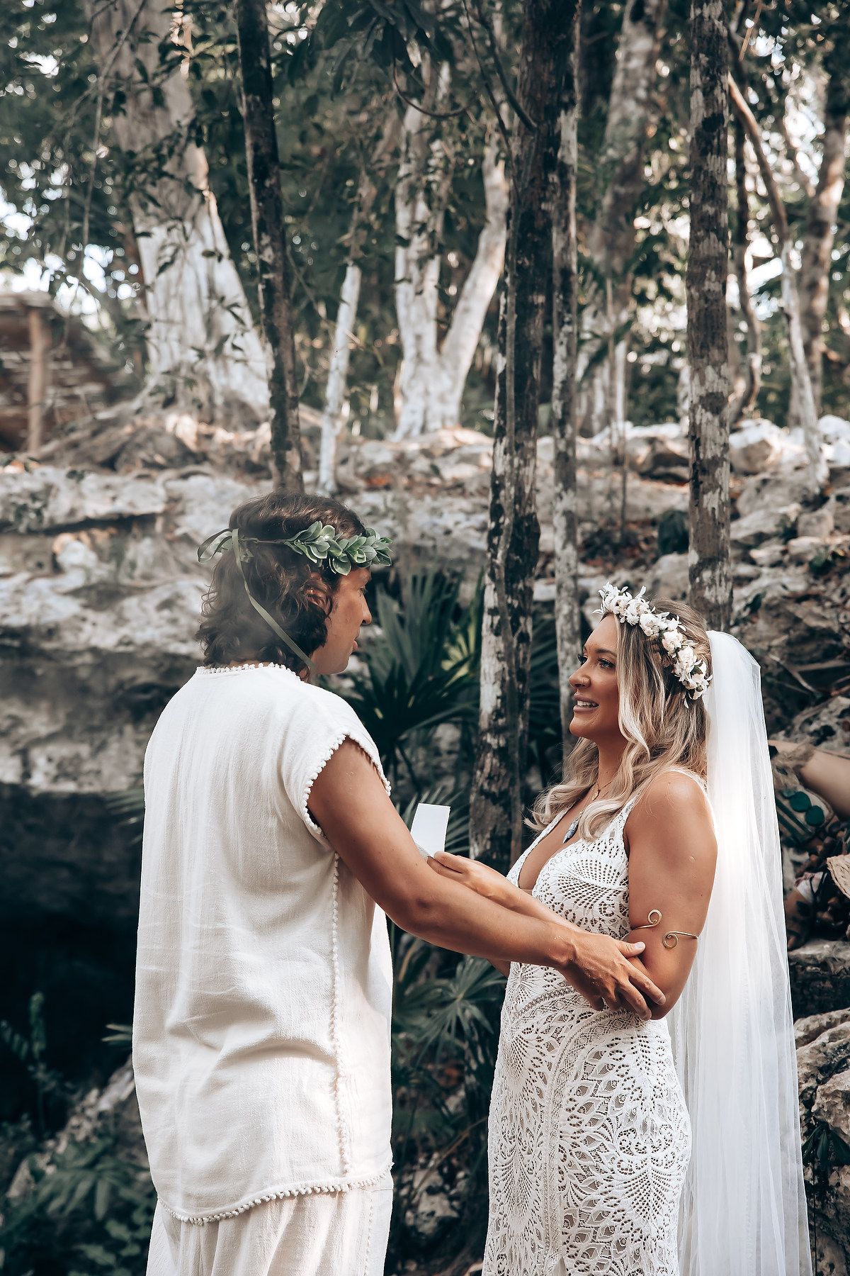 A romantic moment captured between two people in white outfits surrounded by trees.