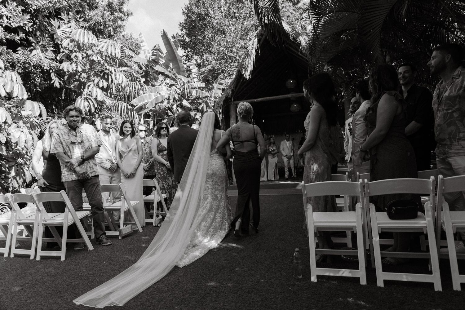 Black and white photo of bride in long veil walking down the aisle with wedding guests watching.