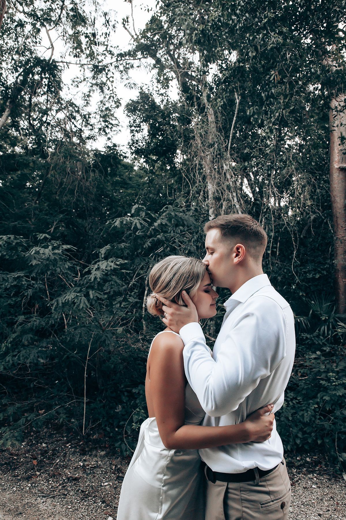 A romantic kiss between newlyweds in a lush forest setting.