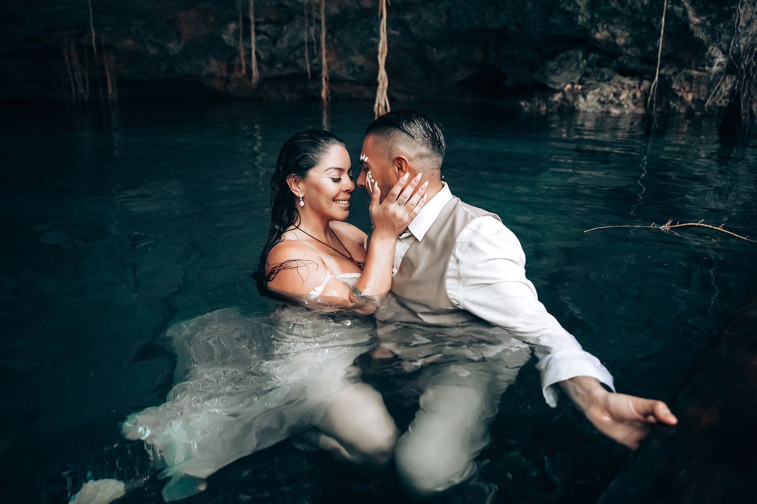 Newlyweds embrace while partially submerged in crystal clear cenote waters.