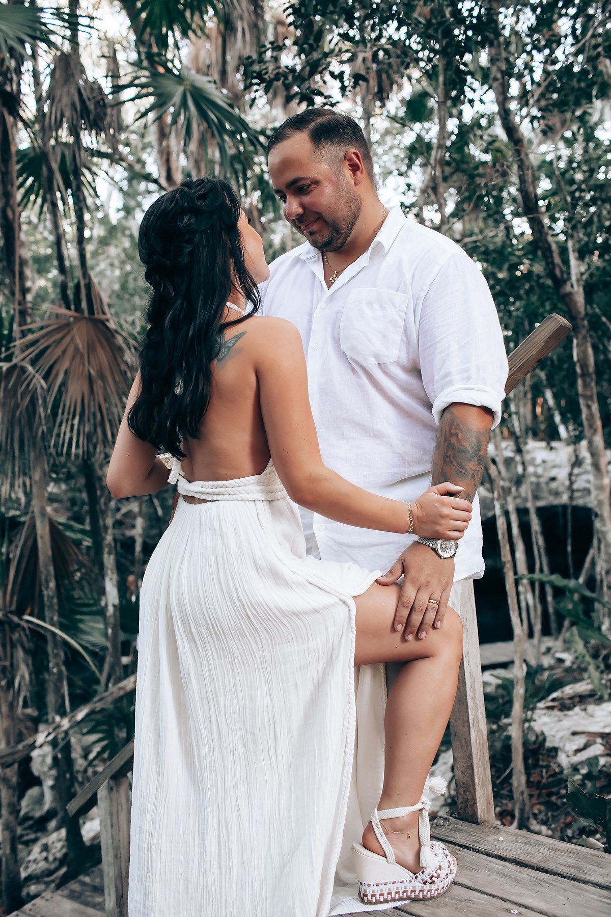Intimate pose on wooden platform surrounded by tropical palm trees and forest.