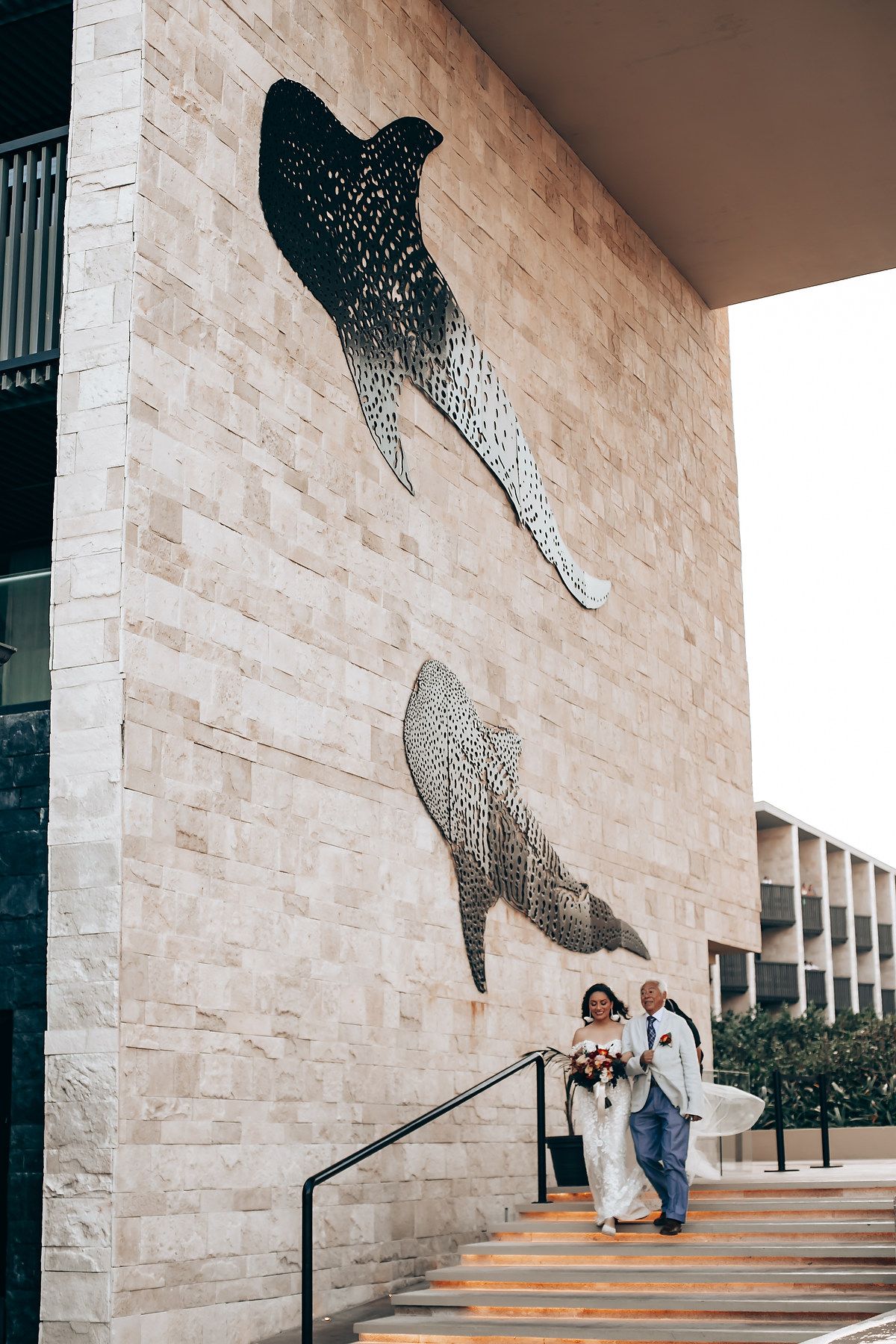 Modern stone building exterior with decorative metal fish sculptures mounted on the wall.