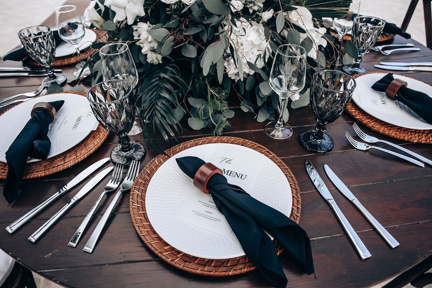 Elegant table settings with eucalyptus decorations and copper charger plates at wedding reception.
