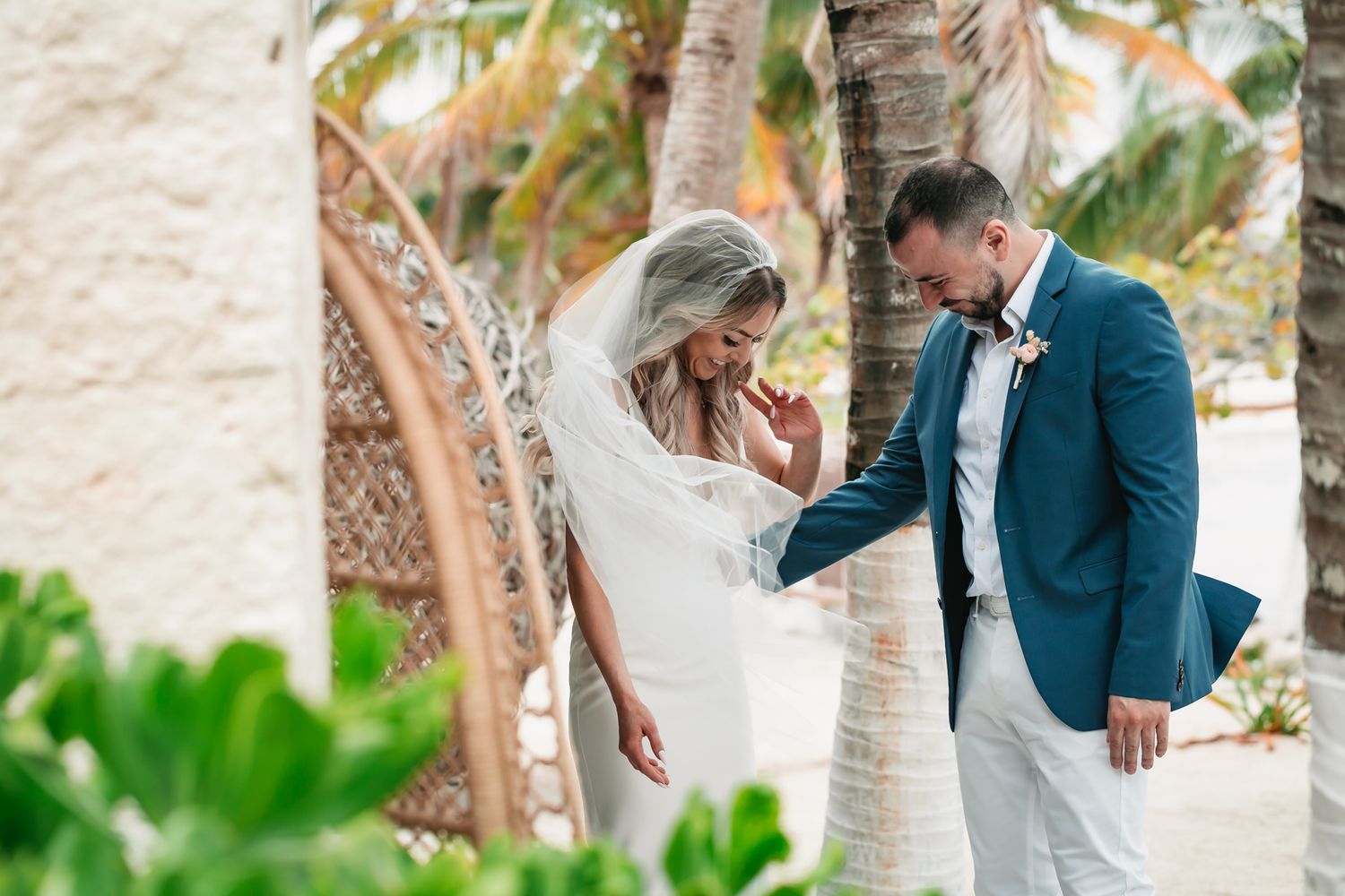 Bride and groom share a tender first look moment among palm trees at a tropical beach wedding.