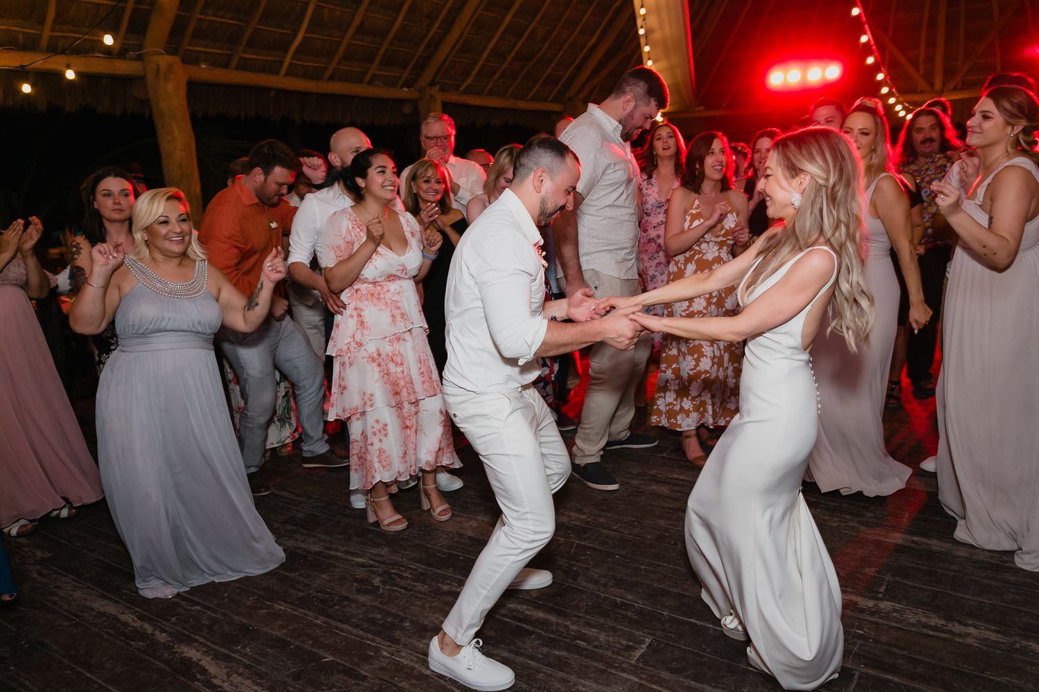 Bride and groom energetically dancing with guests at festive tropical wedding reception party.