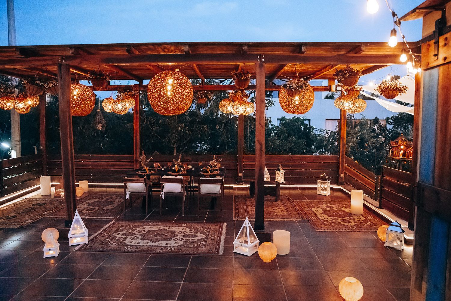 Romantic outdoor wedding reception venue with warm globe lights and wicker pendant lamps at twilight.