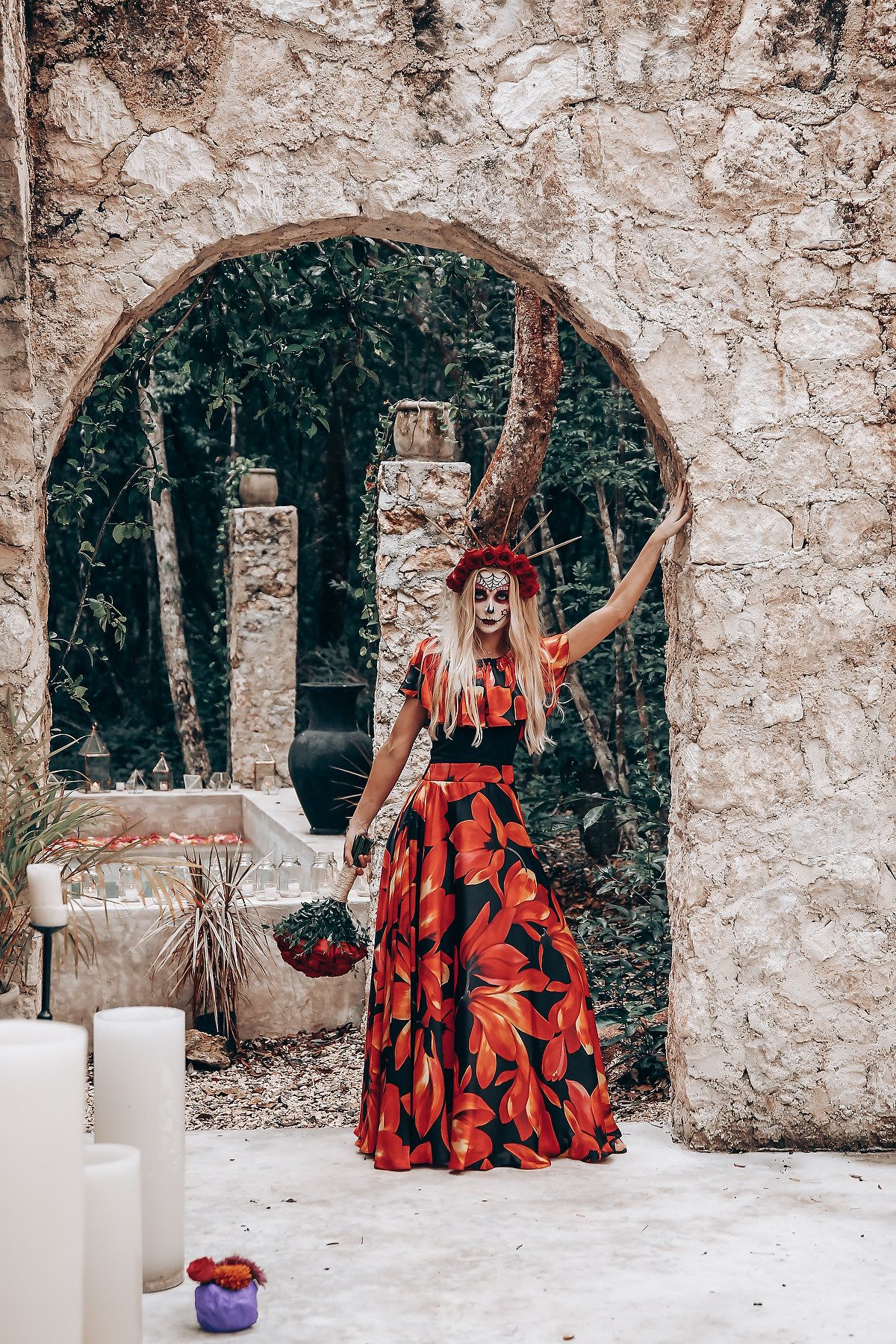 Dramatic red floral dress stands out against stone archway and forest backdrop with white candles.