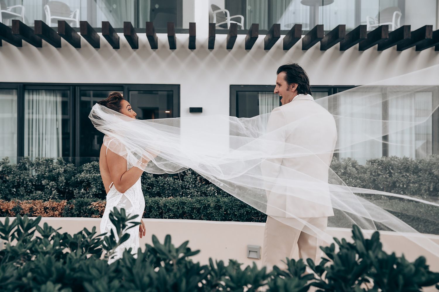 A flowing white wedding dress train trails behind a couple walking through an elegant indoor venue.