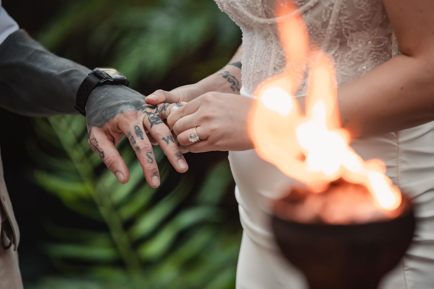 Couple exchanging rings near a tropical torch flame during an outdoor wedding ceremony.