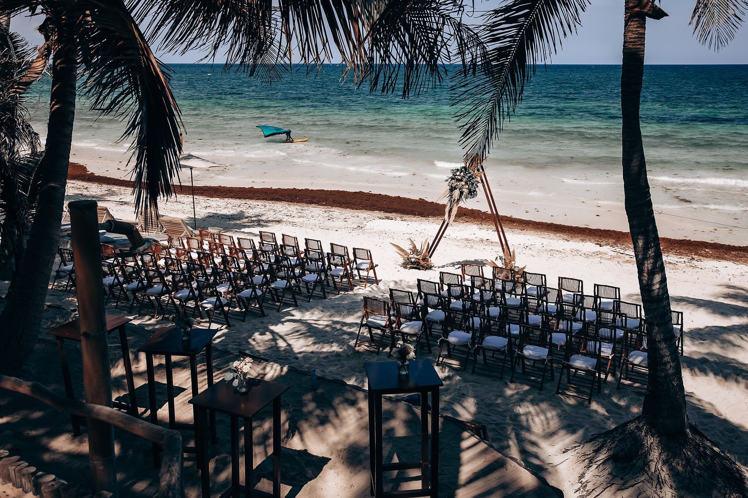 Oceanfront wedding ceremony site with rows of black chairs facing the turquoise water and palm trees.