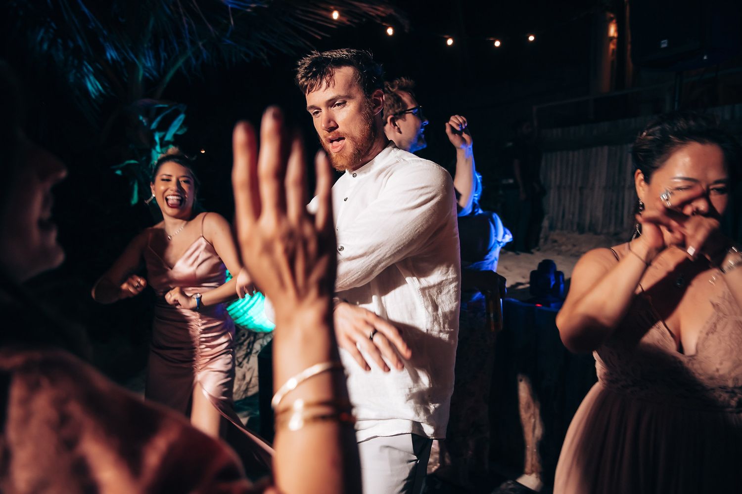 Wedding guests dancing enthusiastically under string lights at a nighttime reception.