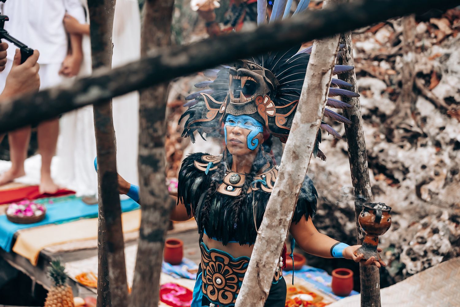 A person wearing face paint and traditional festival attire stands among colorful decorations at an outdoor celebration.