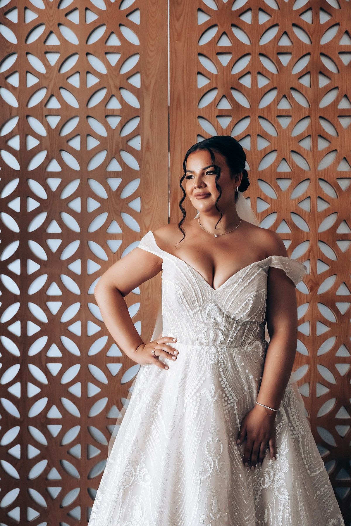 Elegant white wedding dress poses against a decorative wooden lattice wall.