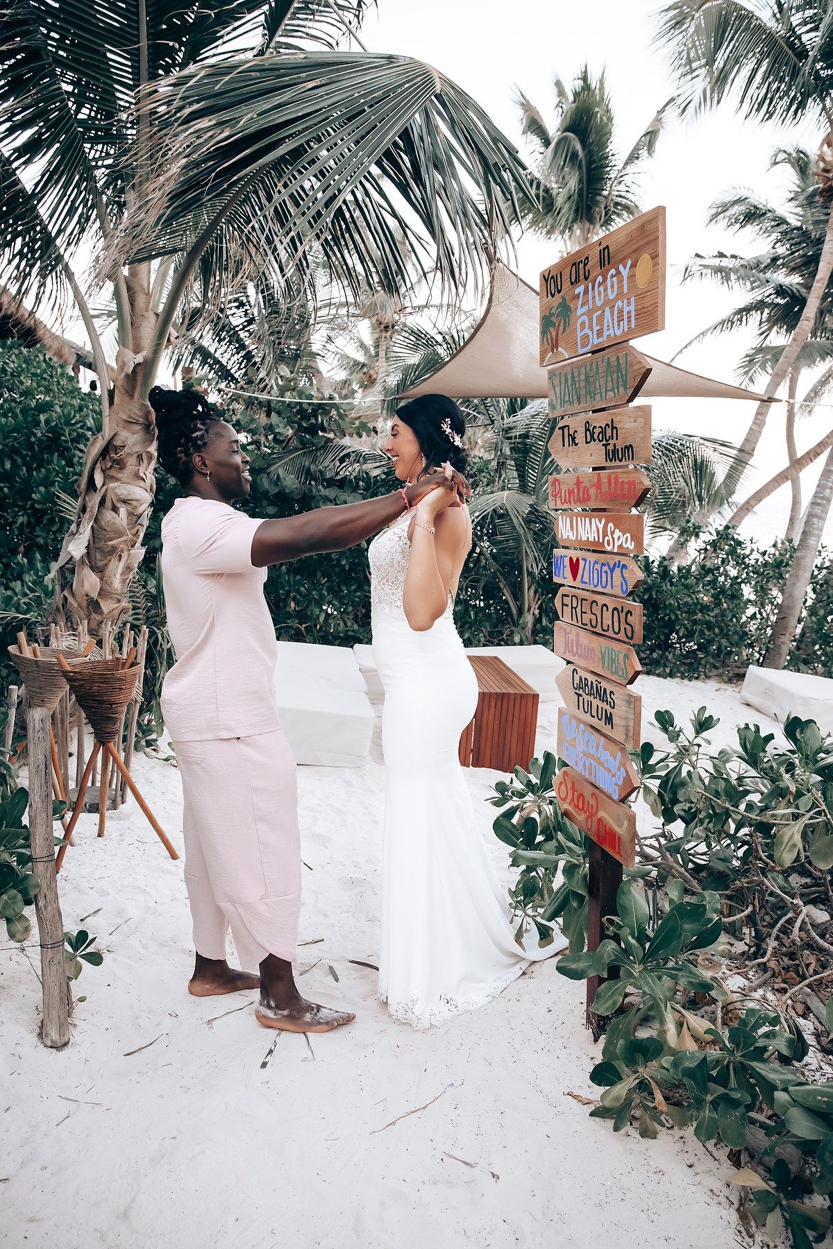 A couple standing under a palm tree with signs pointing to various destinations.