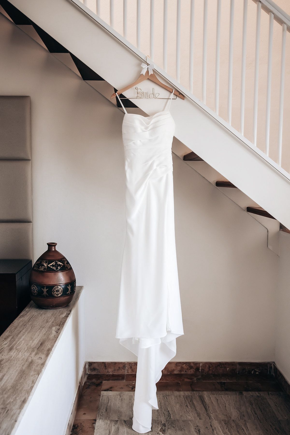 A white wedding dress hangs on a staircase railing.